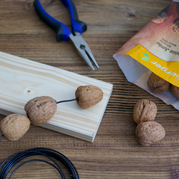 Nüsse auf Draht gefädelt, auf Holzbrett liegend, mit Zange und Verpackung daneben.