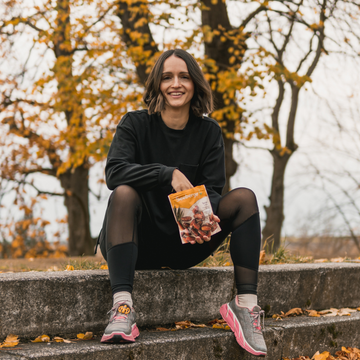 Frau sitzt mit Seeberger-Packung auf Treppe im Herbstpark, umgeben von Laubbäumen.