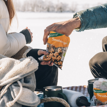 Eine Hand reicht eine Seeberger Nuss-Tüte; Winterlandschaft im Hintergrund.