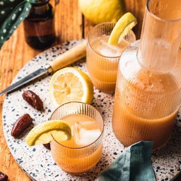 Gläser mit Getränk, Zitrone und Eis stehen auf einem Tisch mit Datteln und Messer.