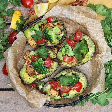 Gefüllte Avocadohälften mit Tofu, Brokkoli und Tomaten, auf Papier in einem Korb.